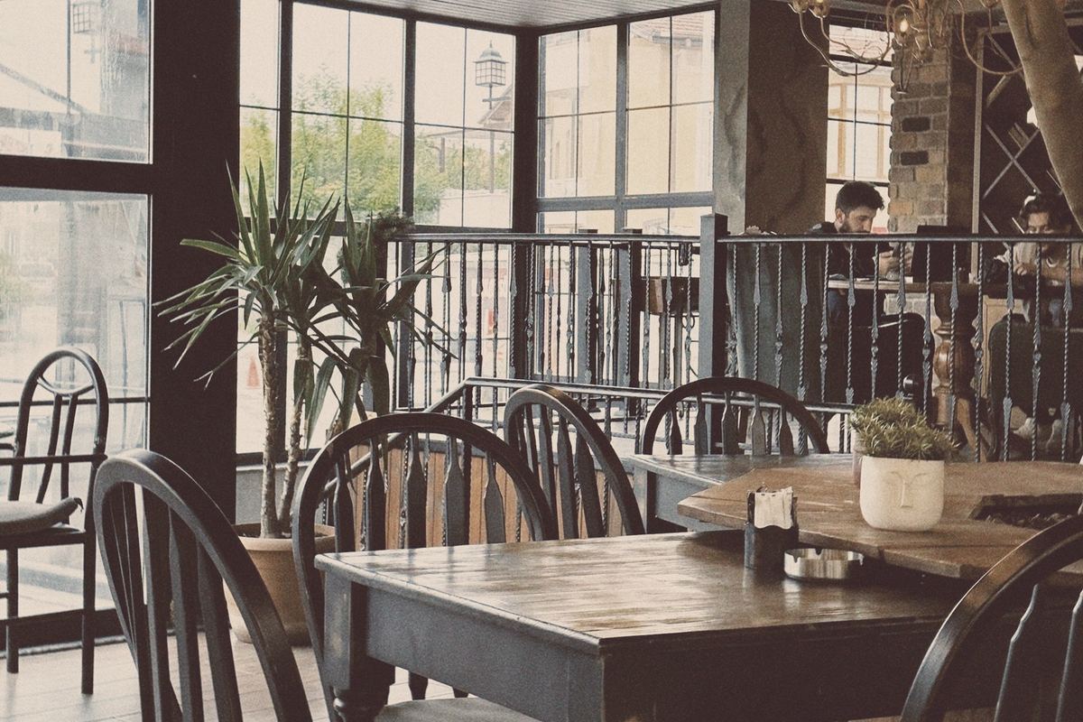 Wooden tables and chairs by tall windows in a small restaurant