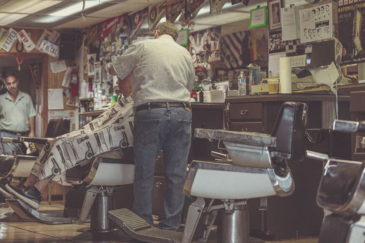 A barber cutting a customer's hair in a small, busy barbershop